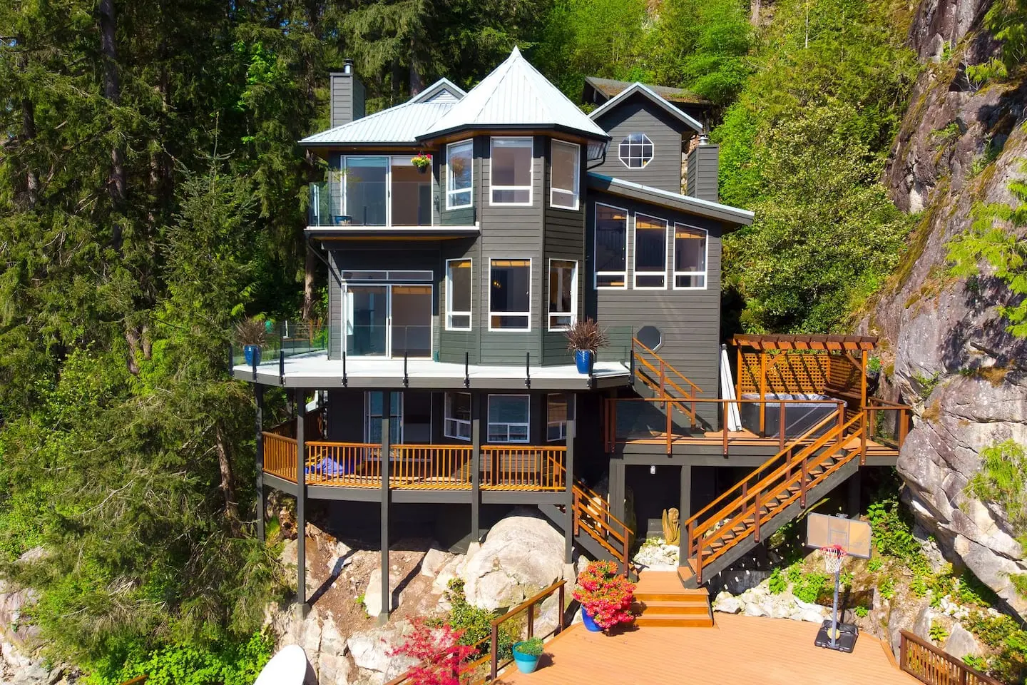 Multi-level grey house with wraparound decks set against a rock bluff