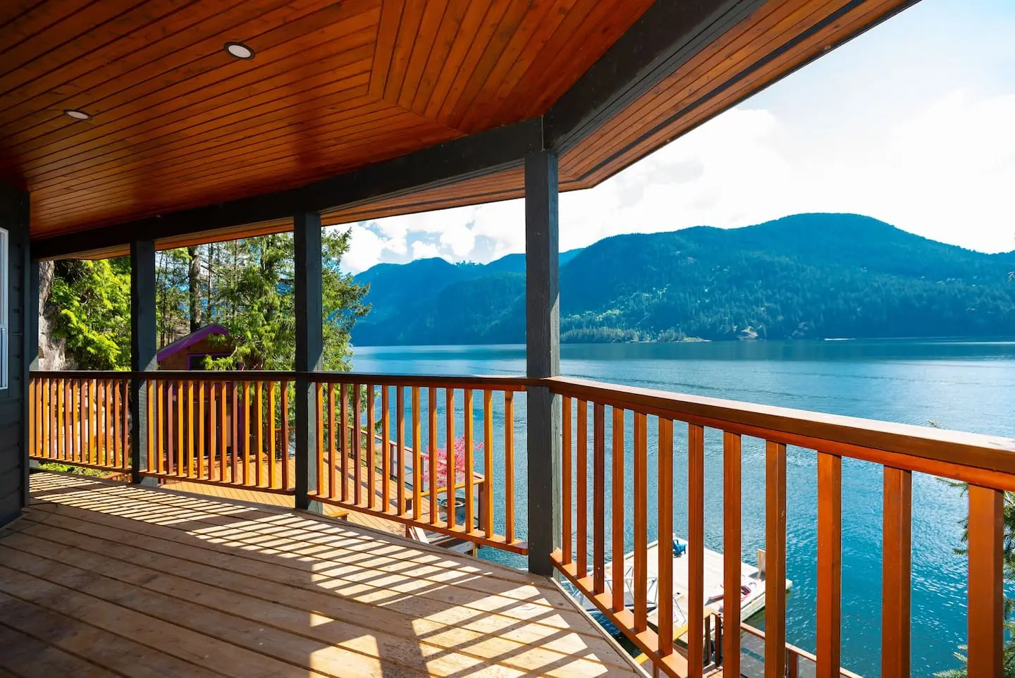 Covered deck with wood railing overlooking the water and mountains